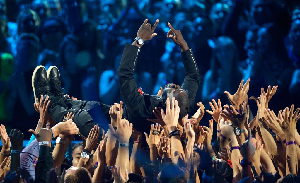 Overhead shot of Kevin Hart standing center-stage in a sold-out arena, spotlight isolating him among 18,000 fans