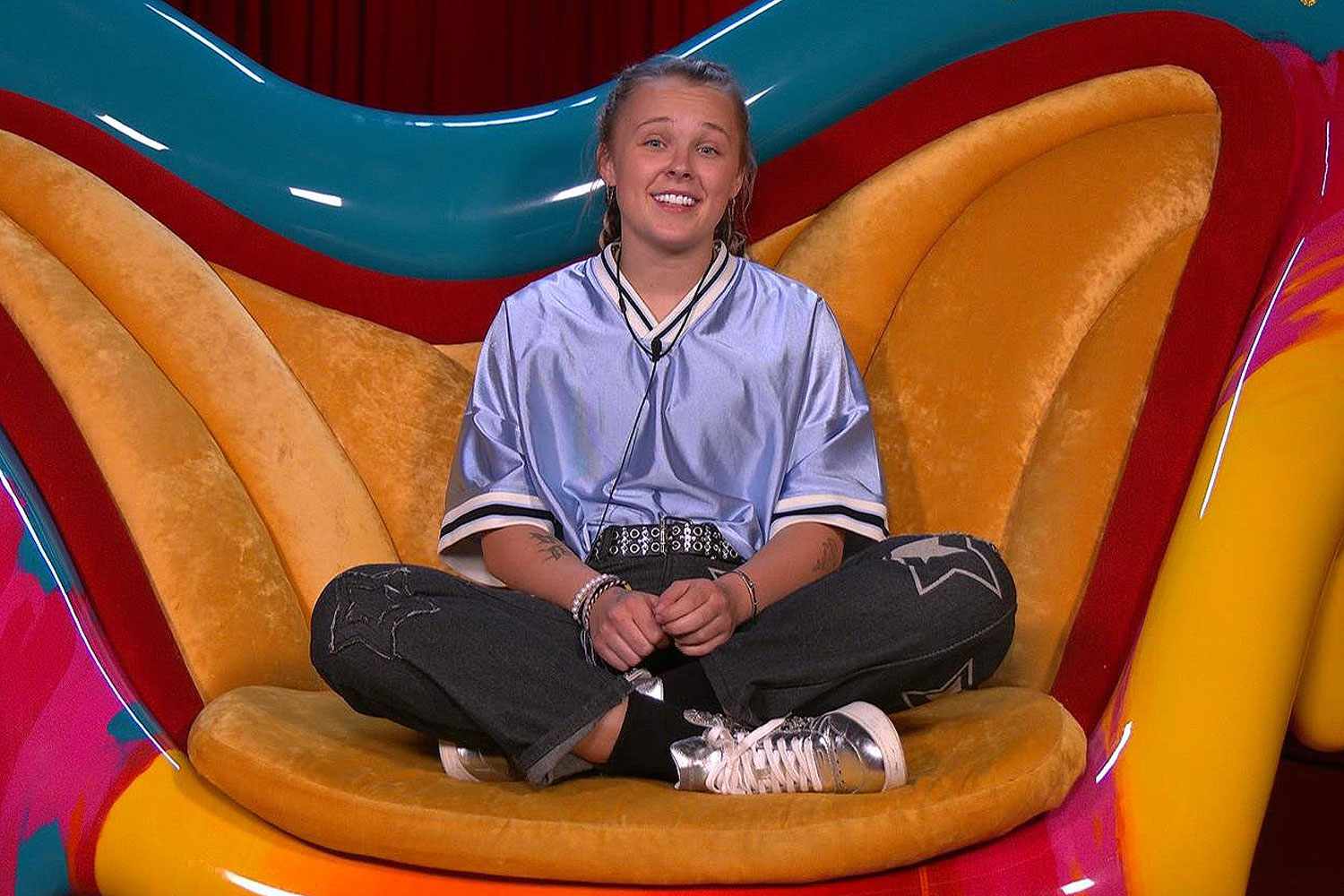 JoJo Siwa sitting in the Diary Room chair on Celebrity Big Brother, hands animatedly describing her feelings
